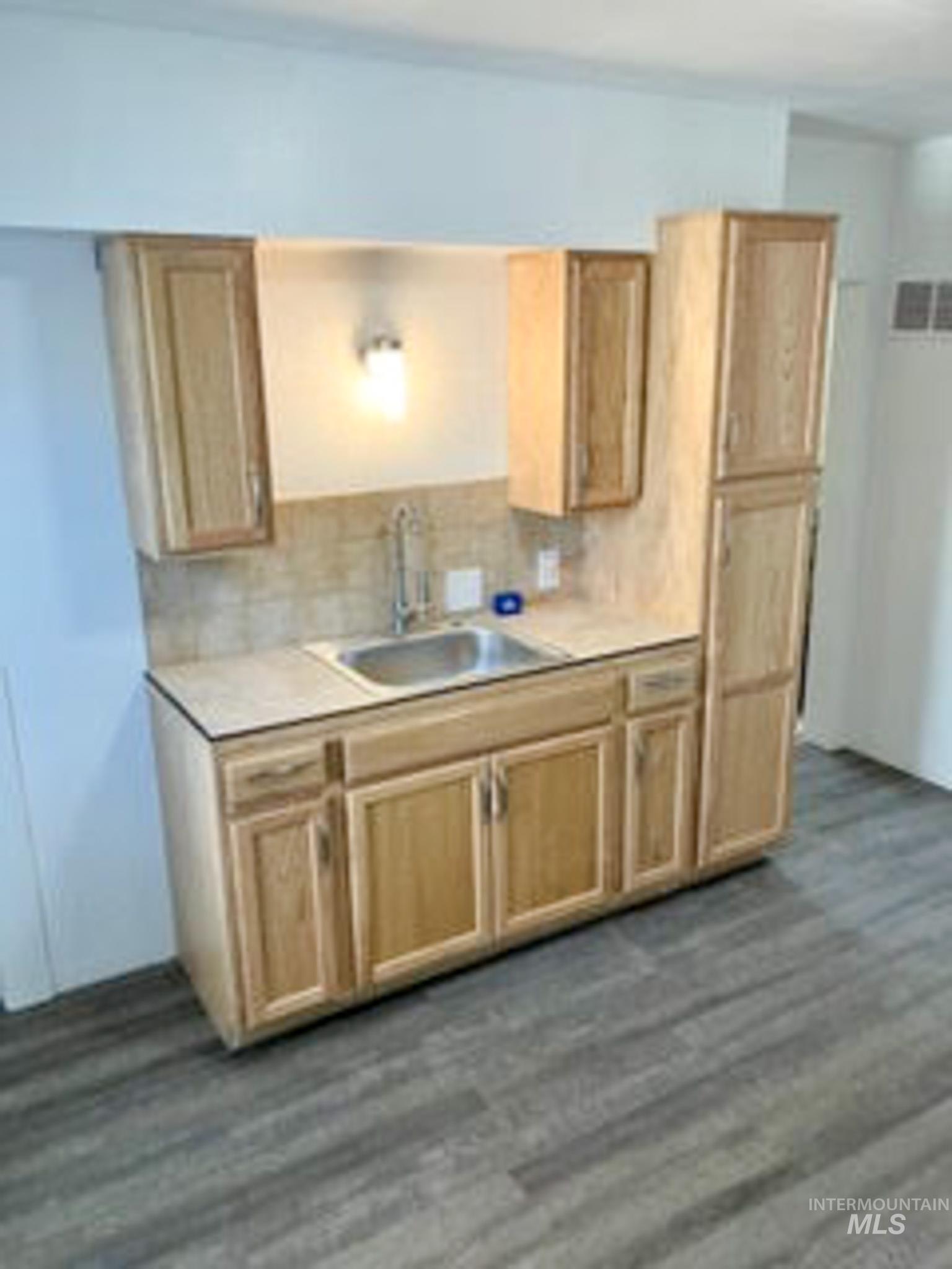 Kitchen with light brown cabinets, dark wood-style floors, decorative backsplash, and light countertops