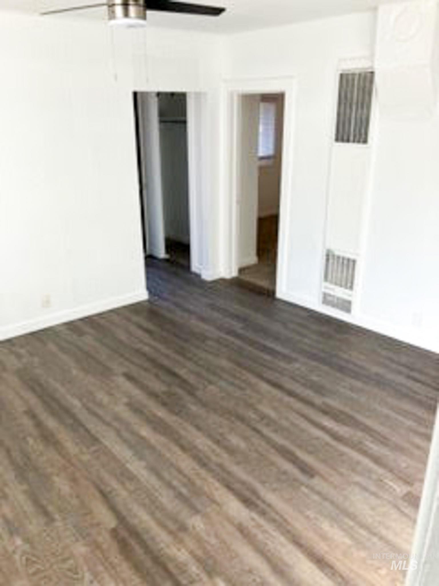 Unfurnished room featuring dark wood-style flooring, ceiling fan, and a heating unit