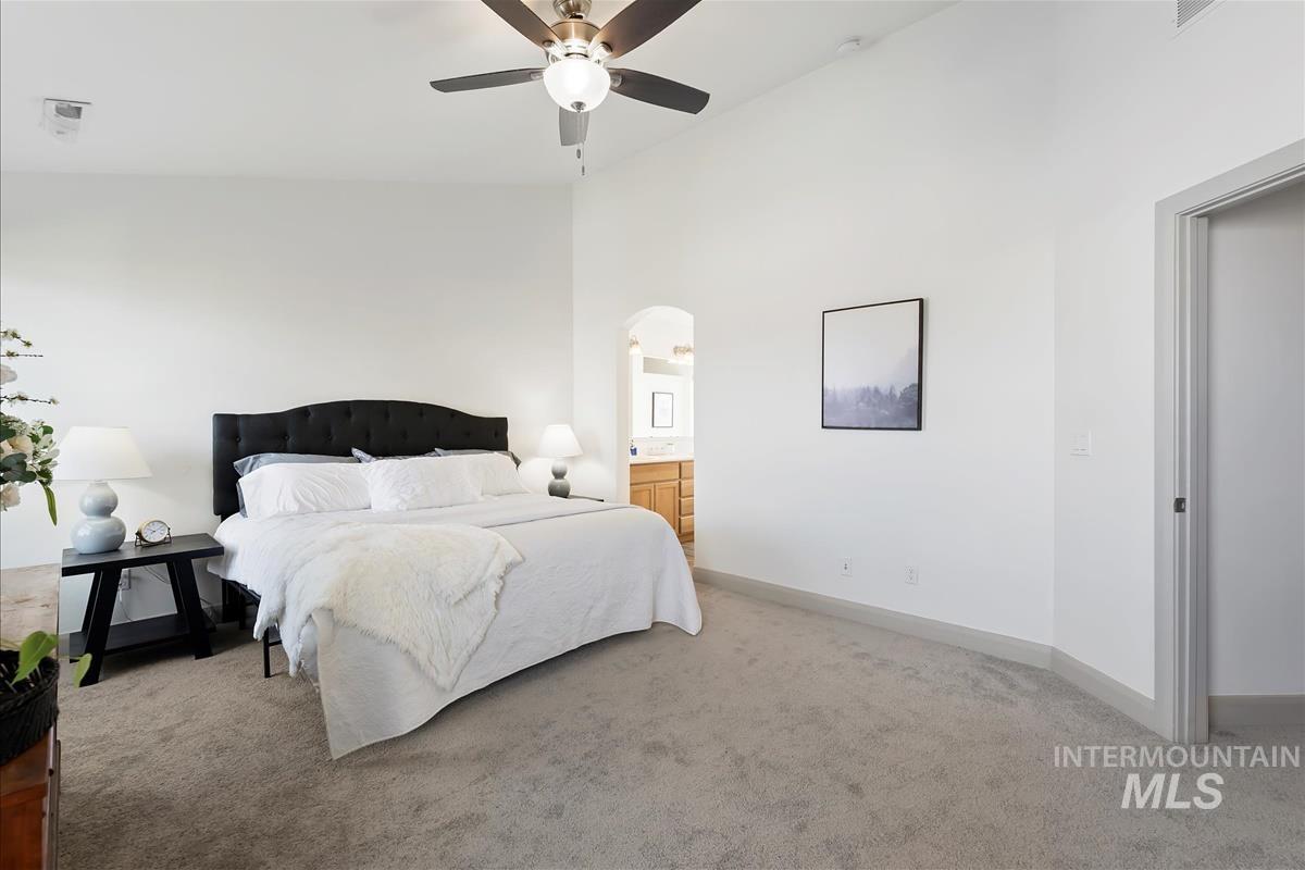 Carpeted bedroom with a ceiling fan, arched walkways, high vaulted ceiling, and ensuite bath