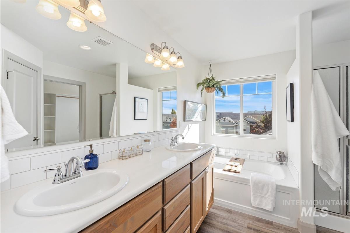 Full bathroom featuring double vanity, a shower stall, light wood-type flooring, and decorative backsplash
