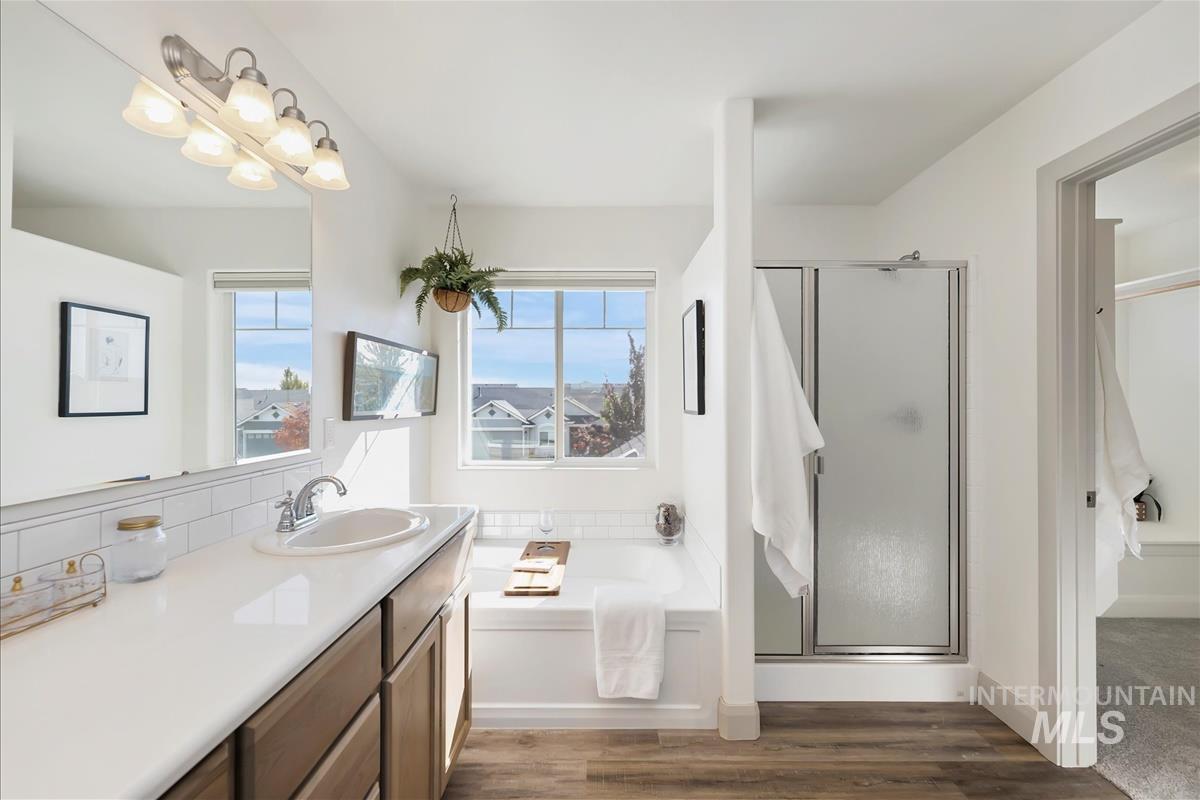Full bath featuring a bath, a stall shower, dark wood-style flooring, decorative backsplash, and vanity