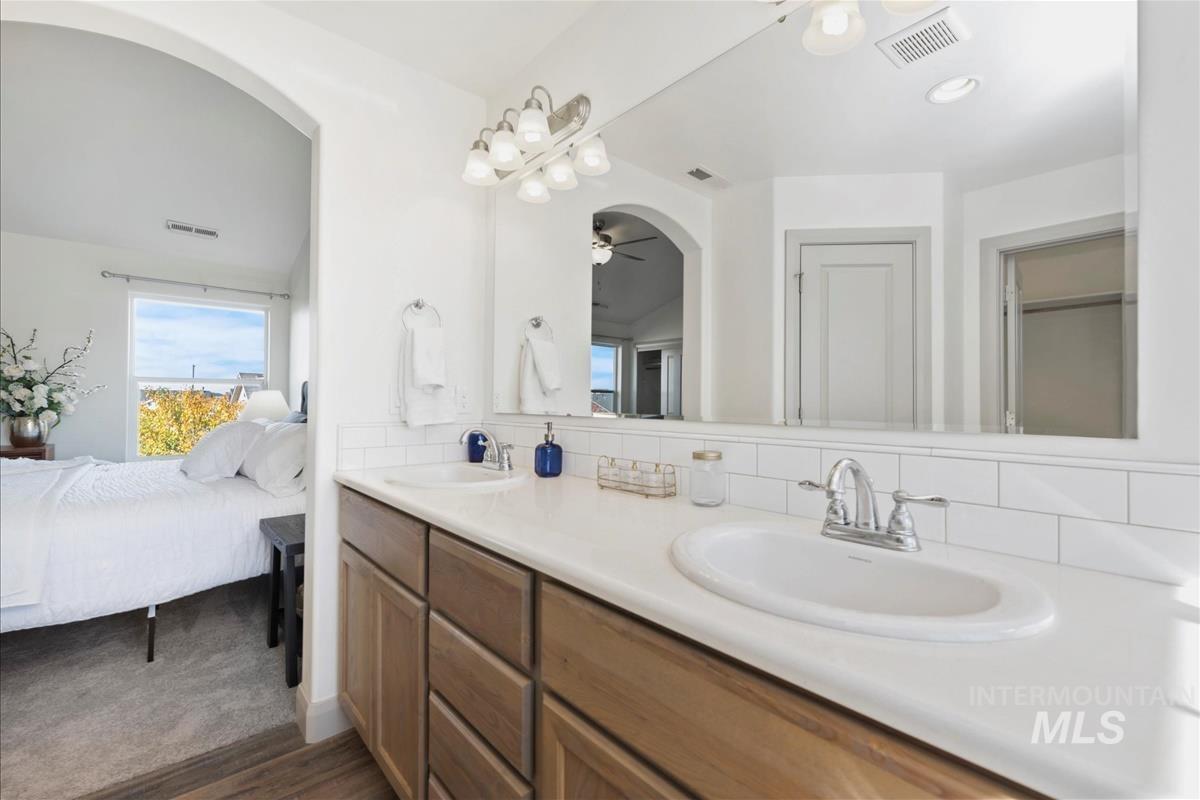 Full bath with backsplash, double vanity, connected bathroom, a ceiling fan, and dark wood-style flooring