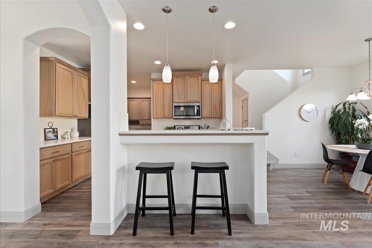 Kitchen featuring a kitchen bar, backsplash, recessed lighting, stainless steel microwave, and light wood finished floors