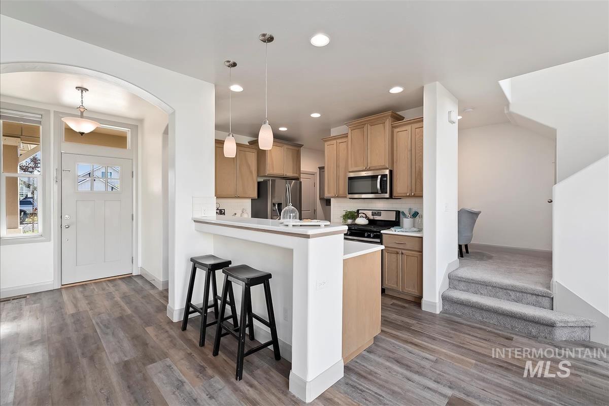 Kitchen with light countertops, a breakfast bar area, pendant lighting, stainless steel appliances, and a peninsula