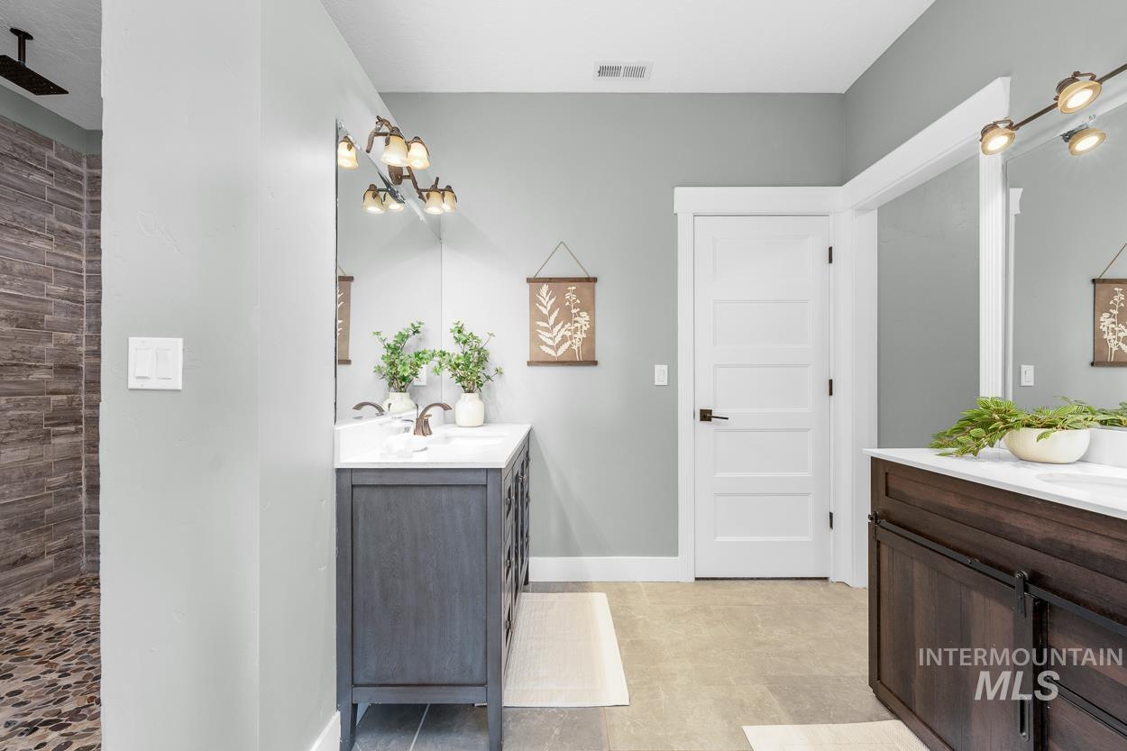 Bathroom featuring two vanities, a tile shower, and light tile patterned floors