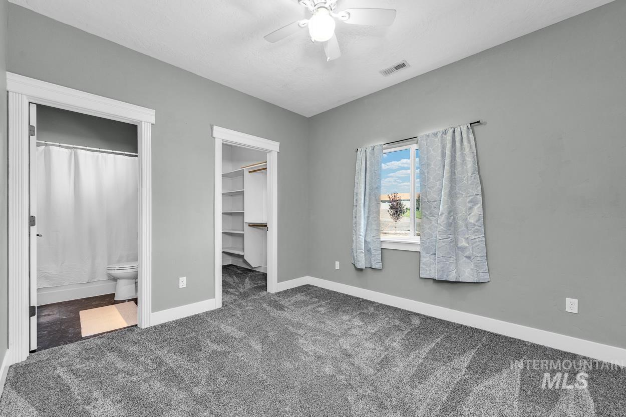 Unfurnished bedroom featuring carpet flooring, a walk in closet, ceiling fan, and connected bathroom