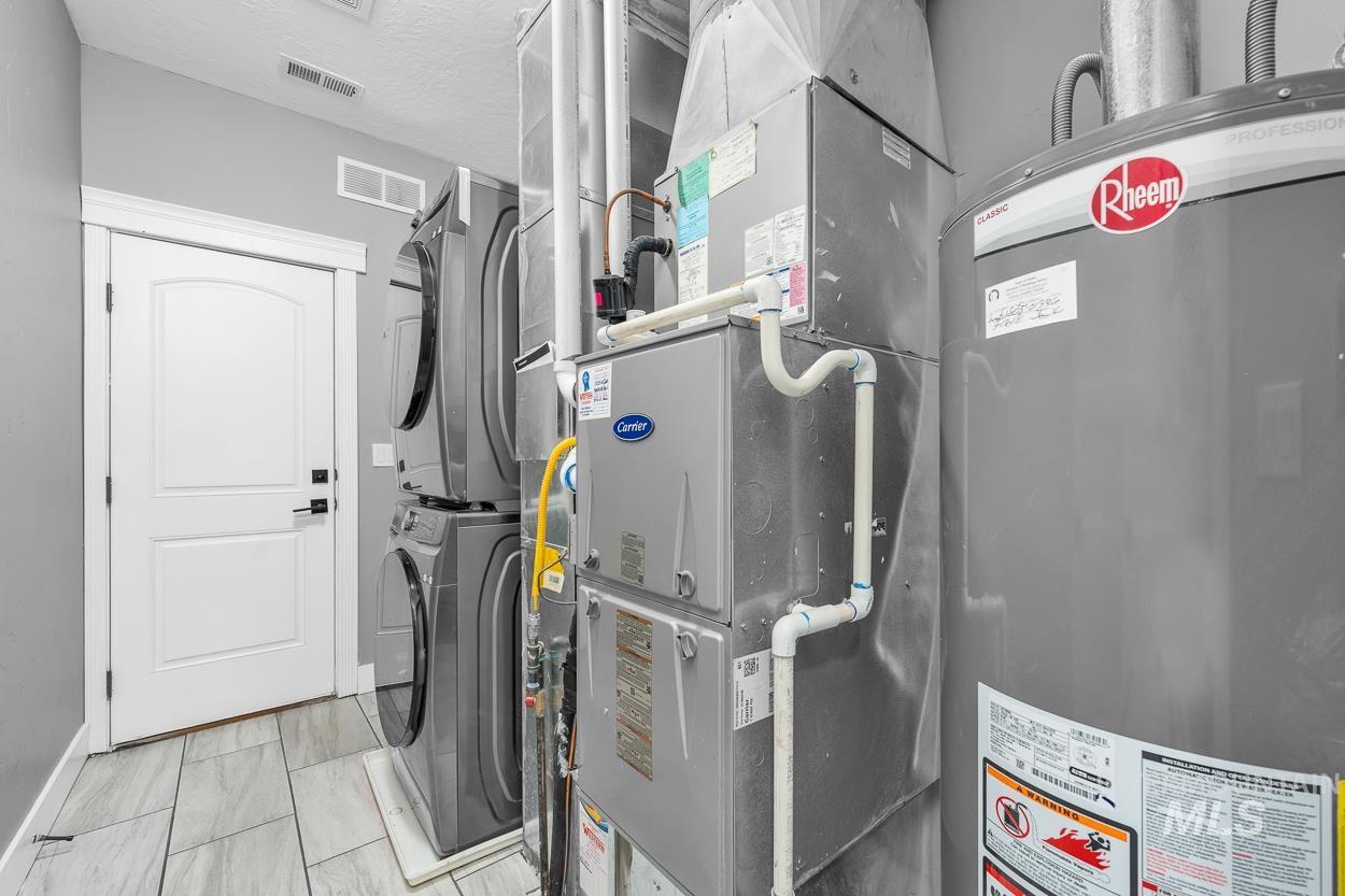 Utilities featuring water heater, heating unit, and estacked washer and dryer