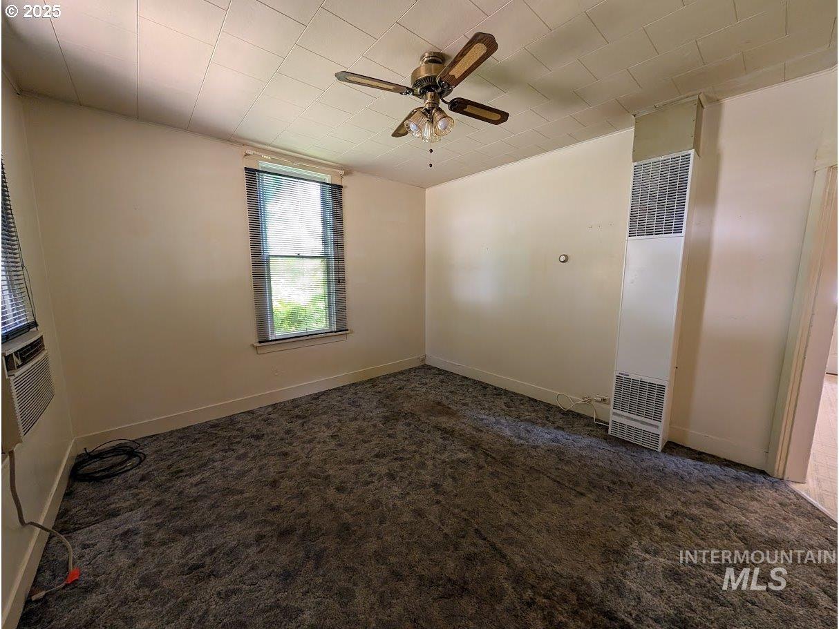 Unfurnished room featuring dark carpet, a heating unit, a ceiling fan, and cooling unit