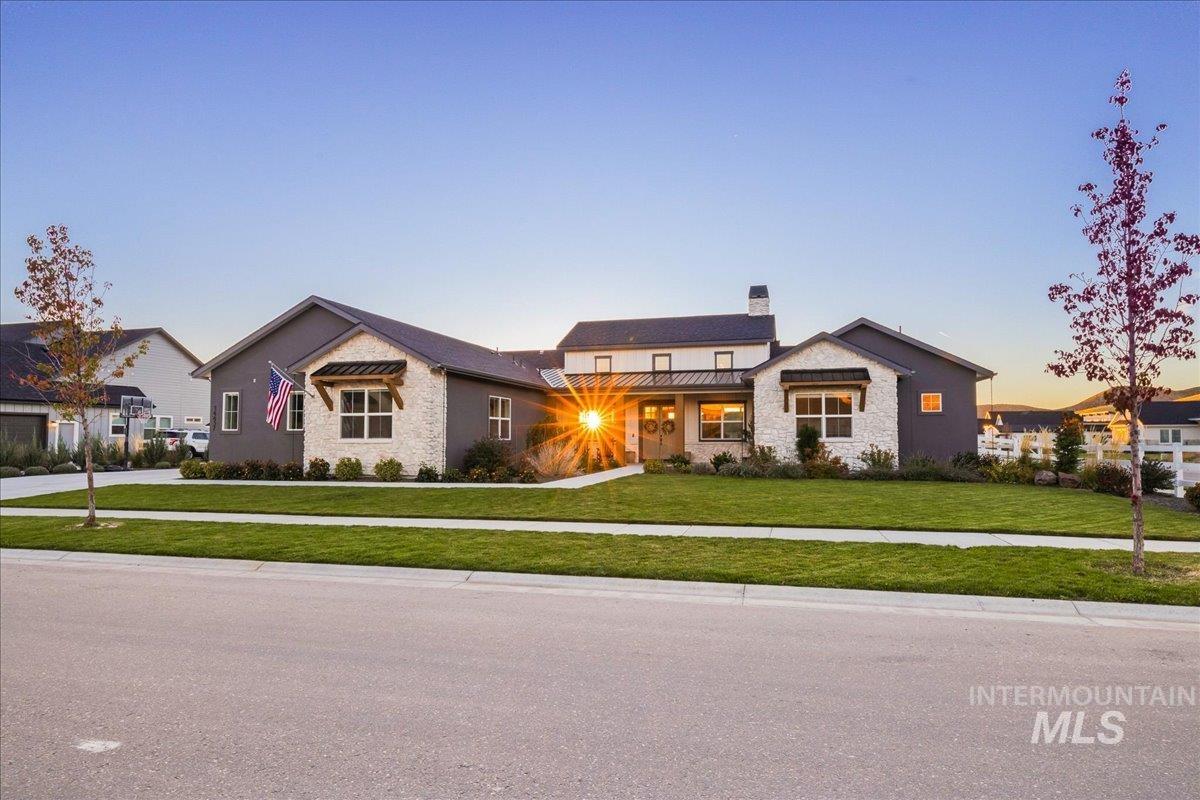 Modern farmhouse style home featuring a lawn, a standing seam roof, stone siding, a chimney, and a metal roof