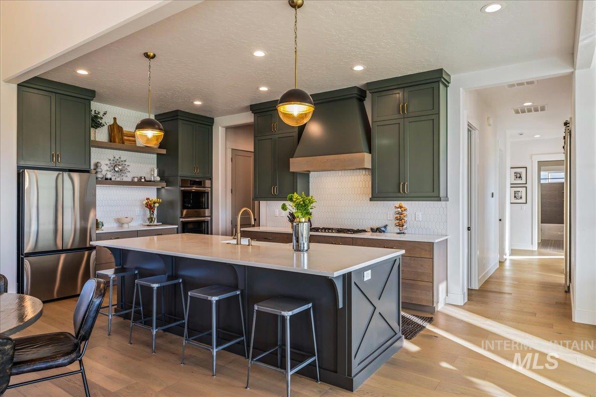 Kitchen featuring backsplash, stainless steel appliances, green cabinets, premium range hood, and recessed lighting