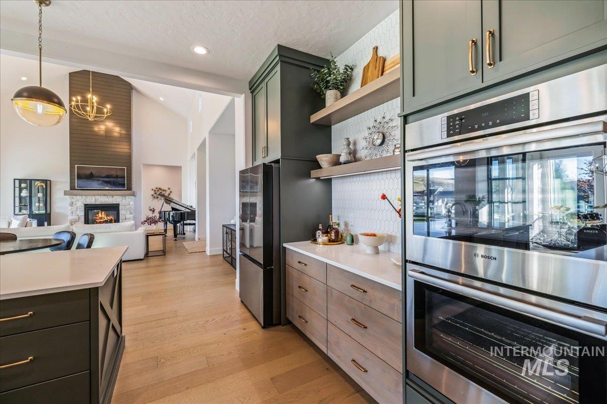 Kitchen featuring stainless steel appliances, open shelves, open floor plan, a stone fireplace, and light wood finished floors
