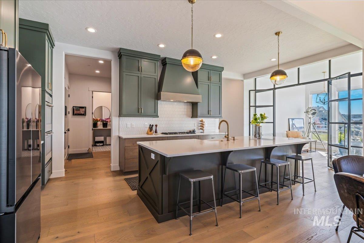 Kitchen with green cabinets, appliances with stainless steel finishes, decorative light fixtures, custom exhaust hood, and a textured ceiling