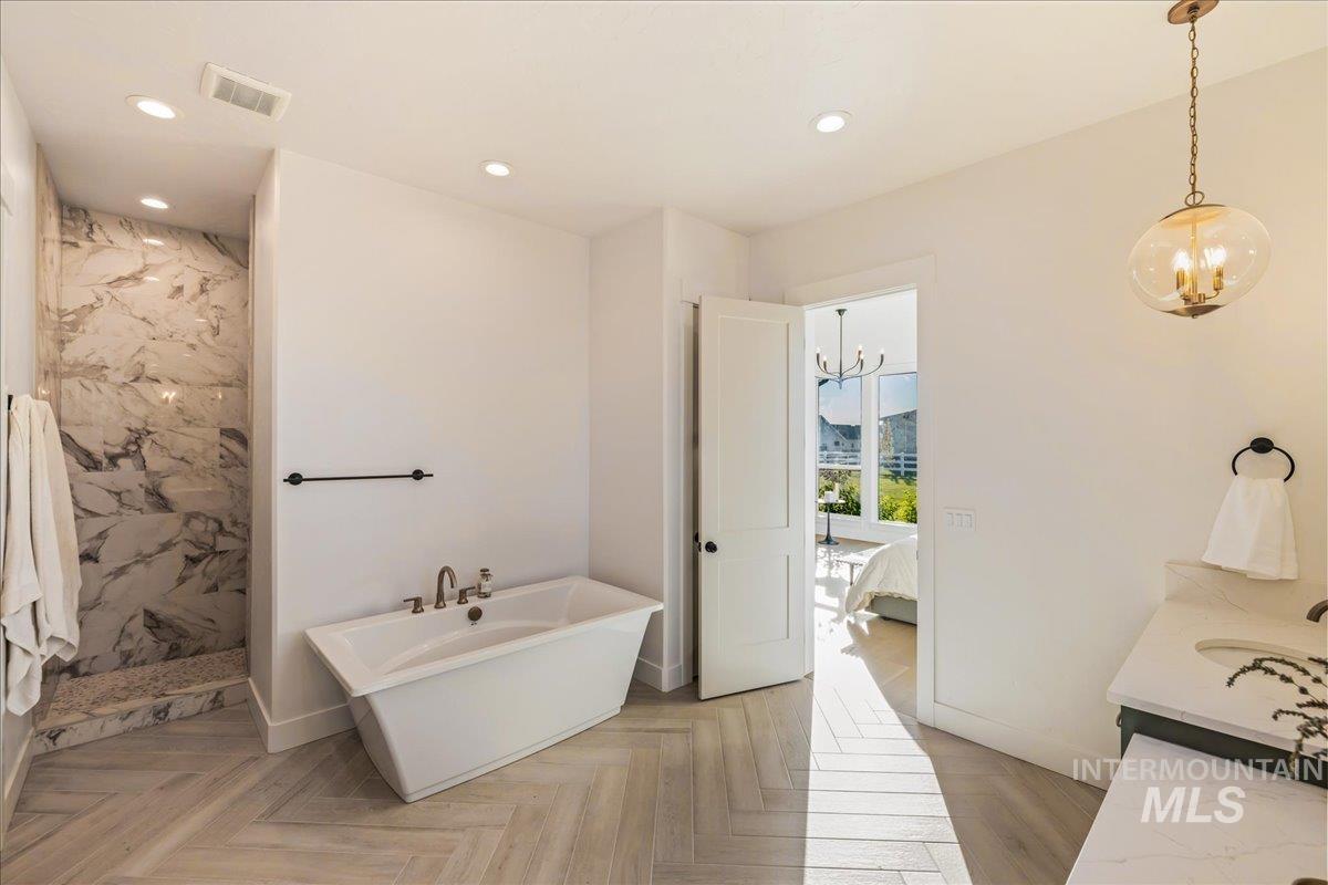 Ensuite bathroom featuring vanity, a soaking tub, recessed lighting, a marble finish shower, and a chandelier