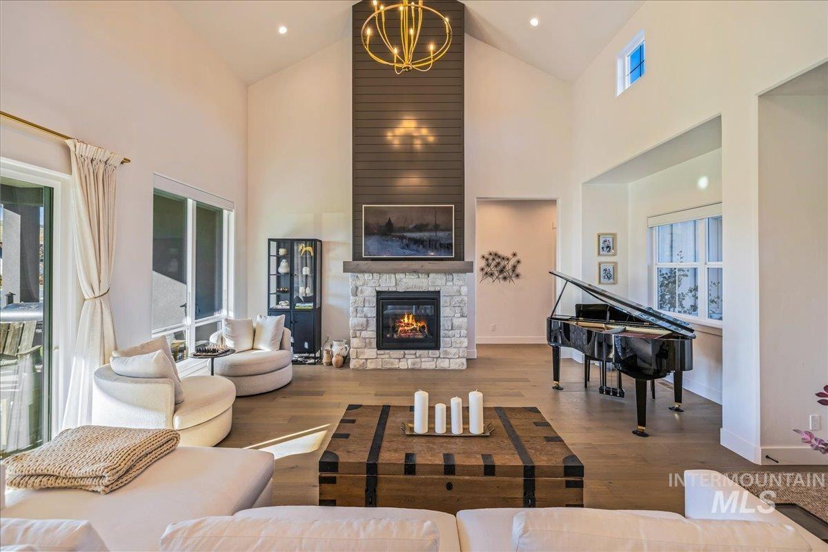Living room featuring high vaulted ceiling, wood finished floors, a chandelier, and a stone fireplace