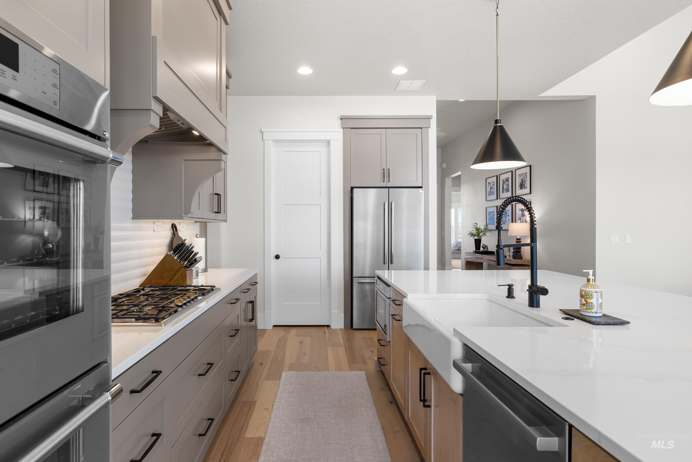 Kitchen with stainless steel appliances, light wood-style floors, decorative light fixtures, gray cabinetry, and light stone counters