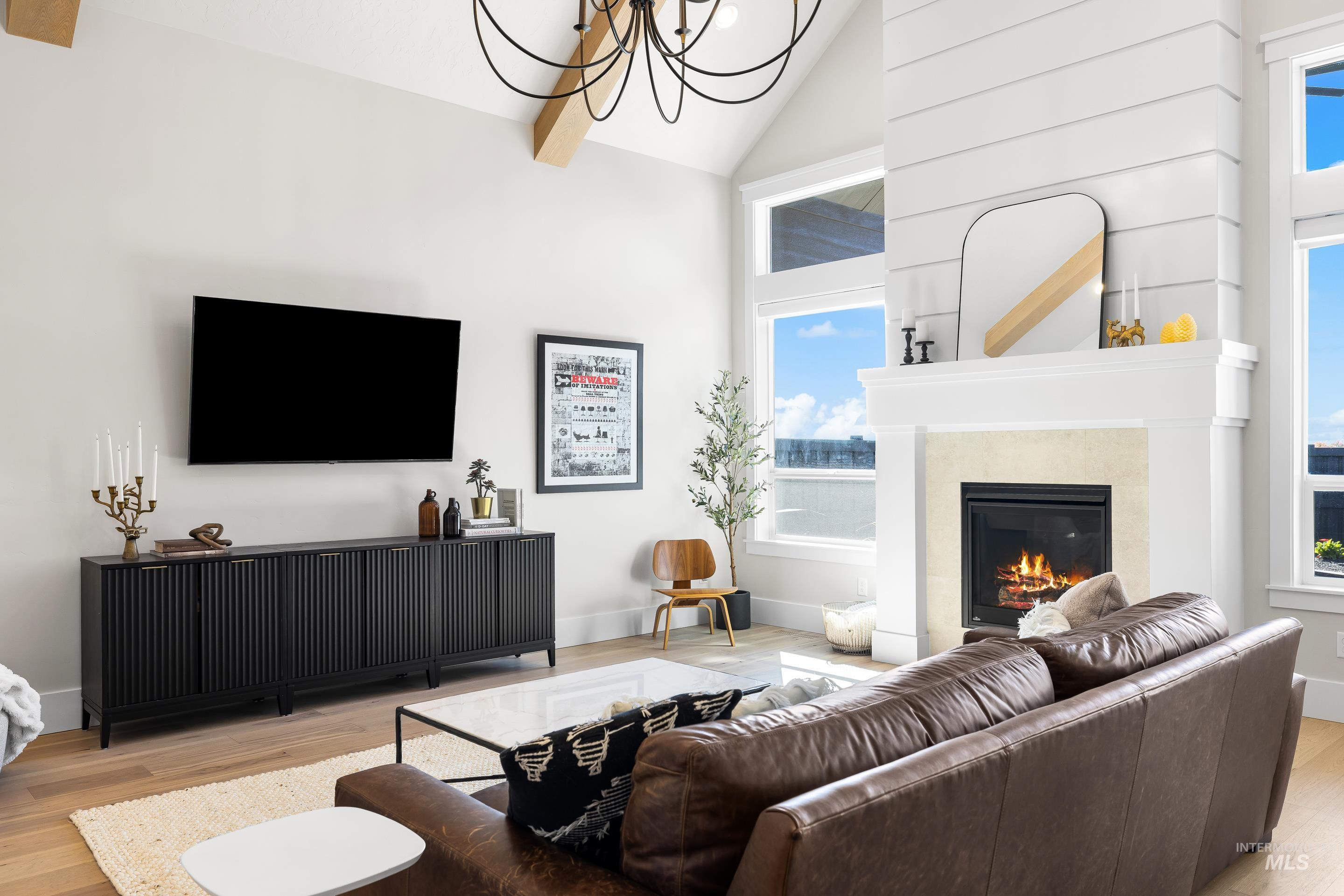 Living area with light wood-style flooring, a glass covered fireplace, high vaulted ceiling, a chandelier, and beam ceiling
