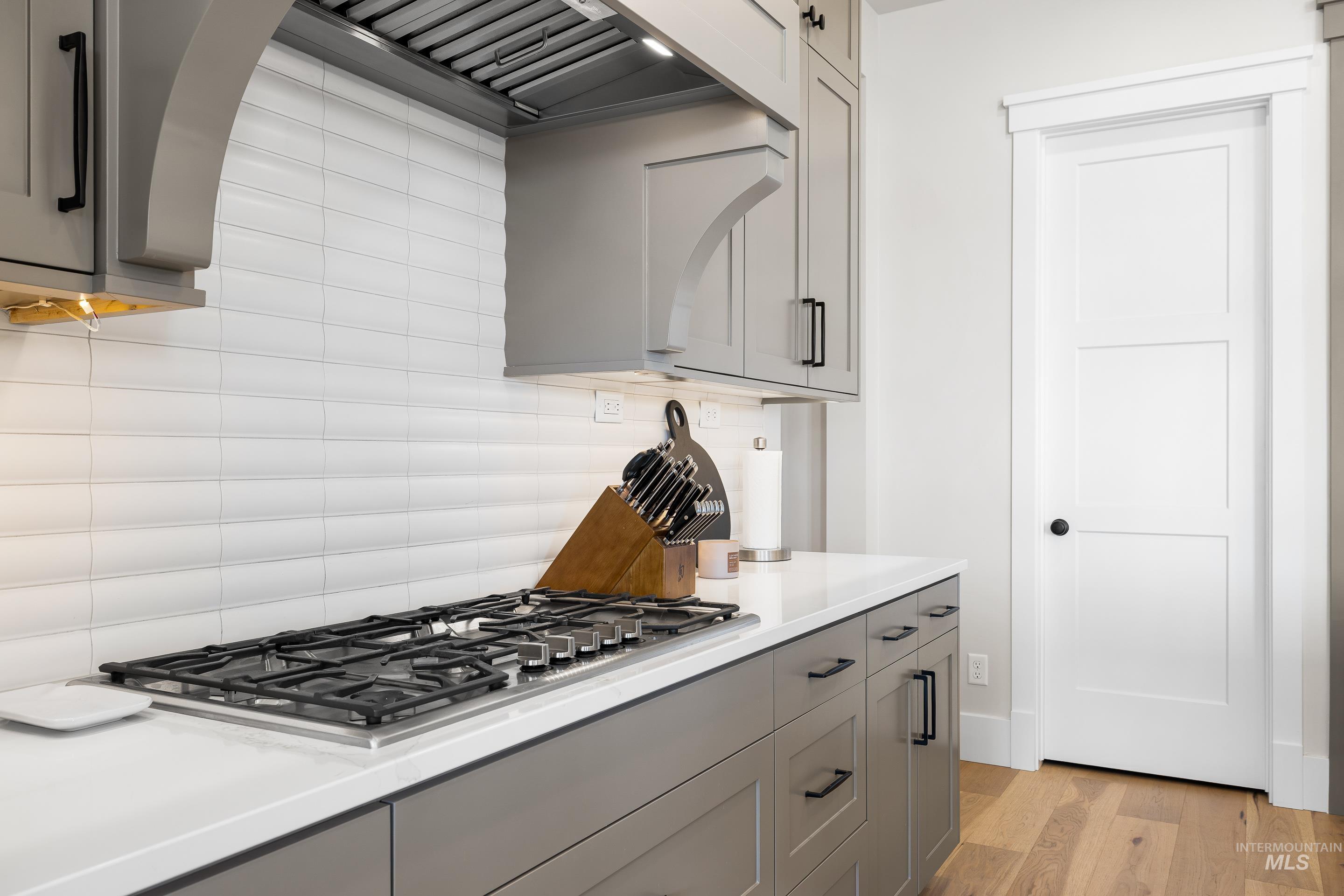 Kitchen with gray cabinetry, decorative backsplash, stainless steel gas cooktop, and light wood finished floors