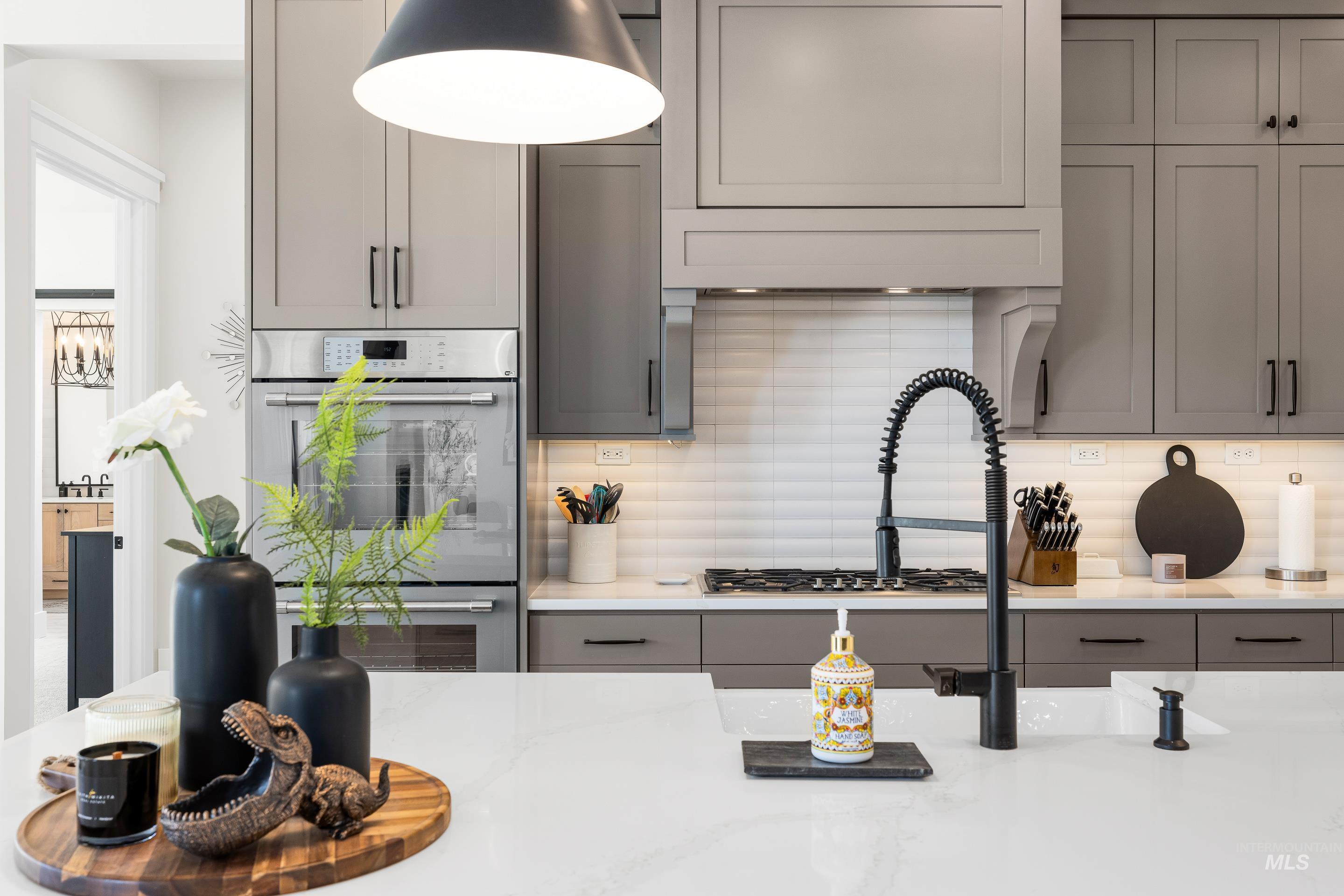 Kitchen with backsplash, gray cabinets, double oven, and light stone counters