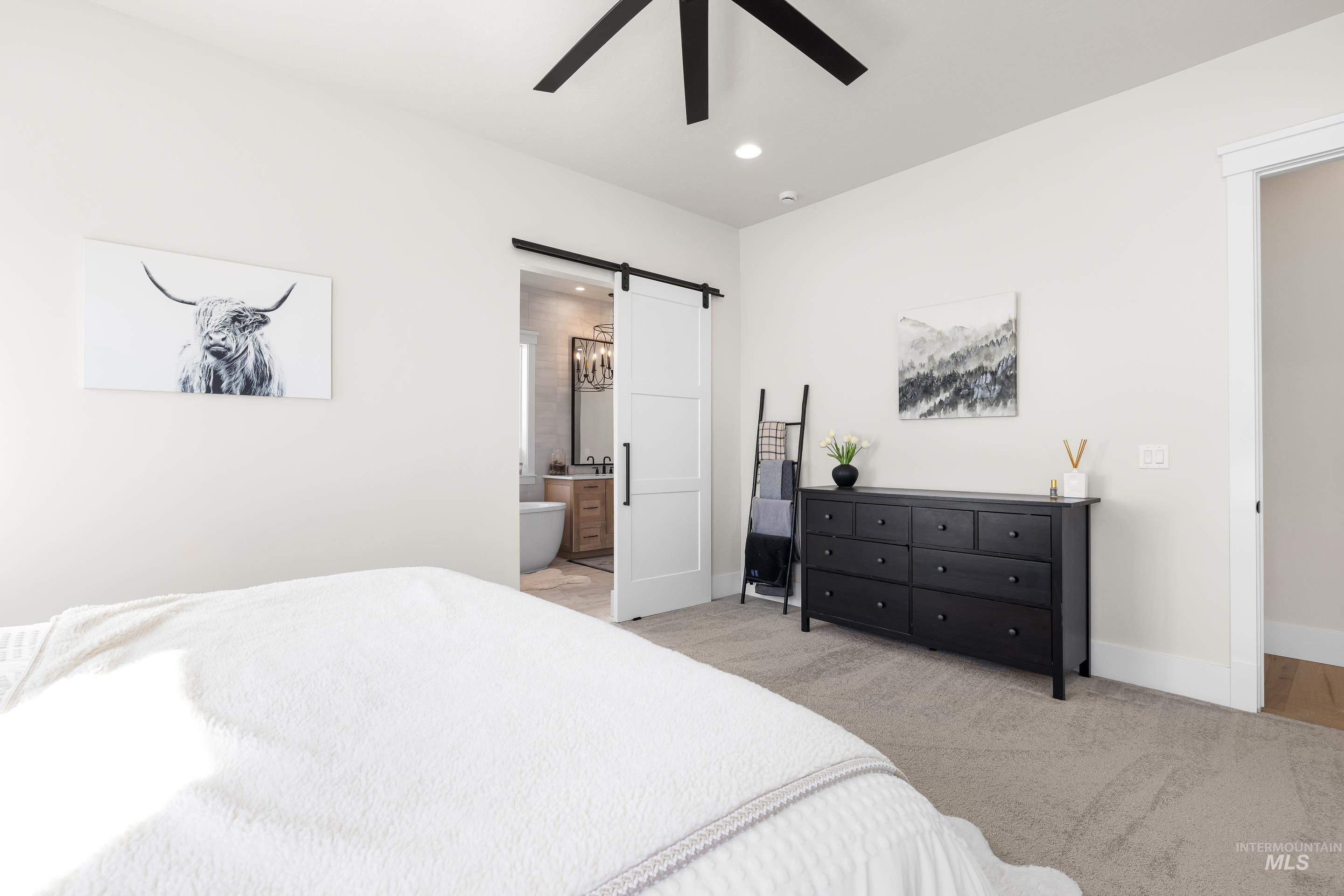 Bedroom featuring a barn door, light colored carpet, recessed lighting, ceiling fan, and ensuite bathroom