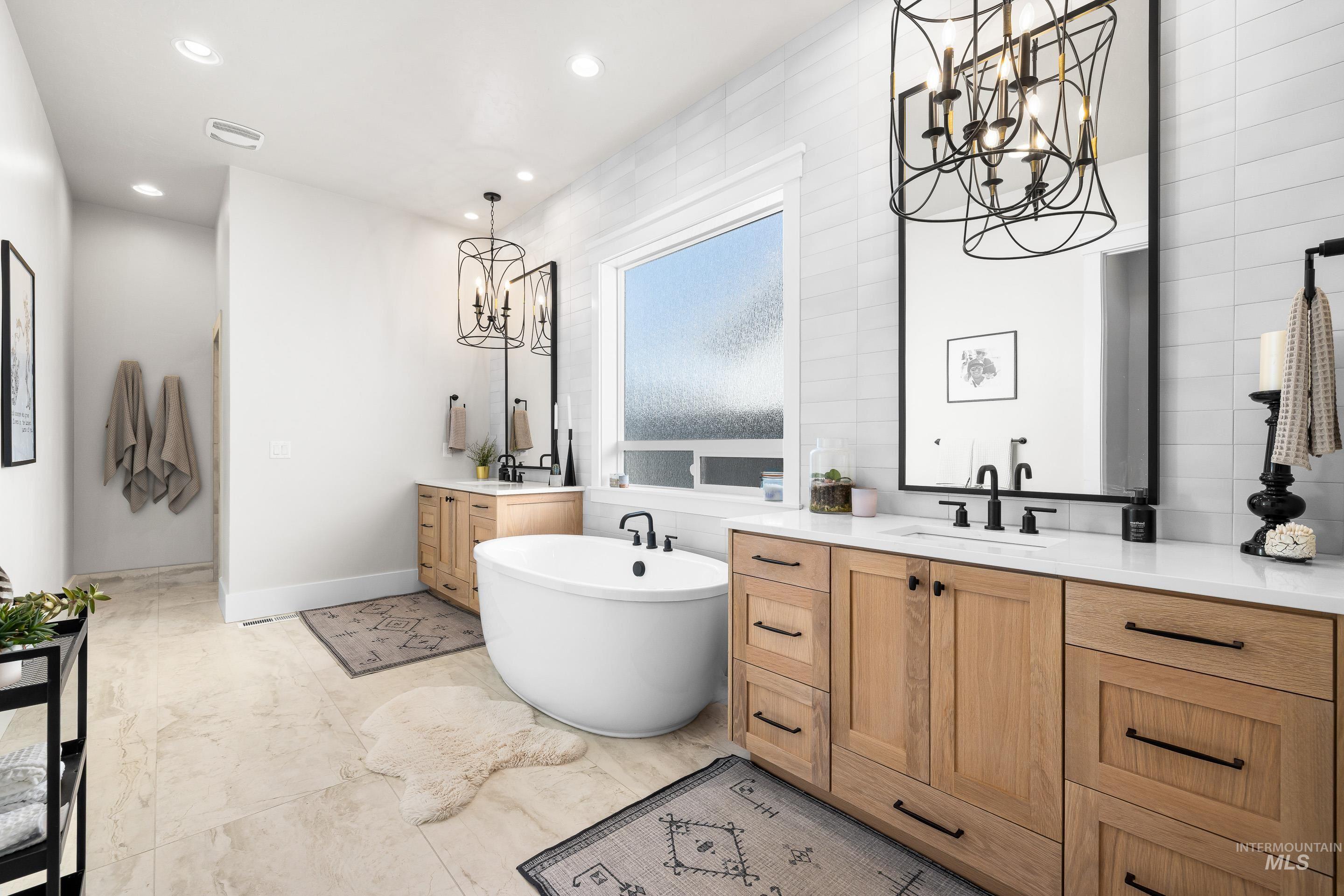 Bathroom with a chandelier, a soaking tub, two vanities, recessed lighting, and tile walls