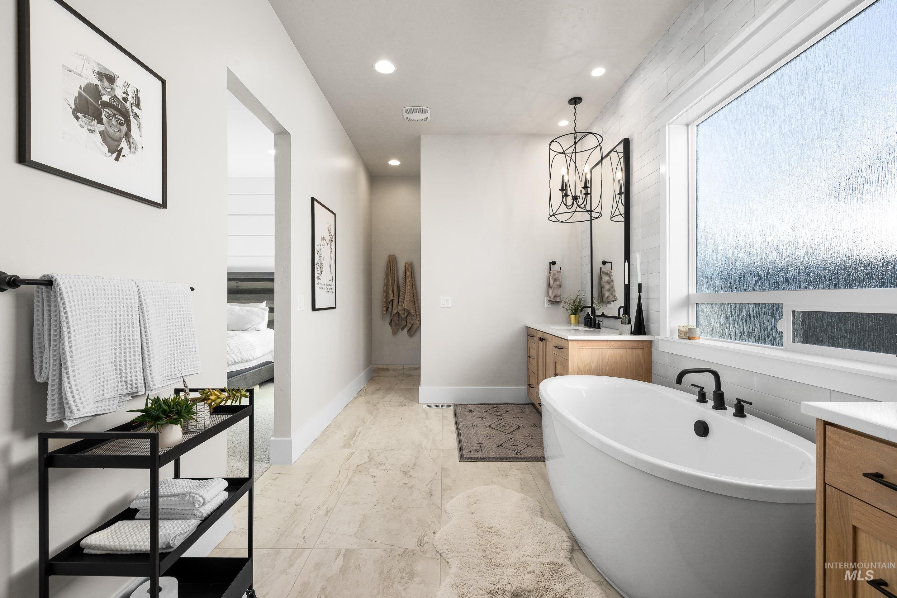 Ensuite bathroom featuring vanity, a freestanding bath, recessed lighting, and a chandelier