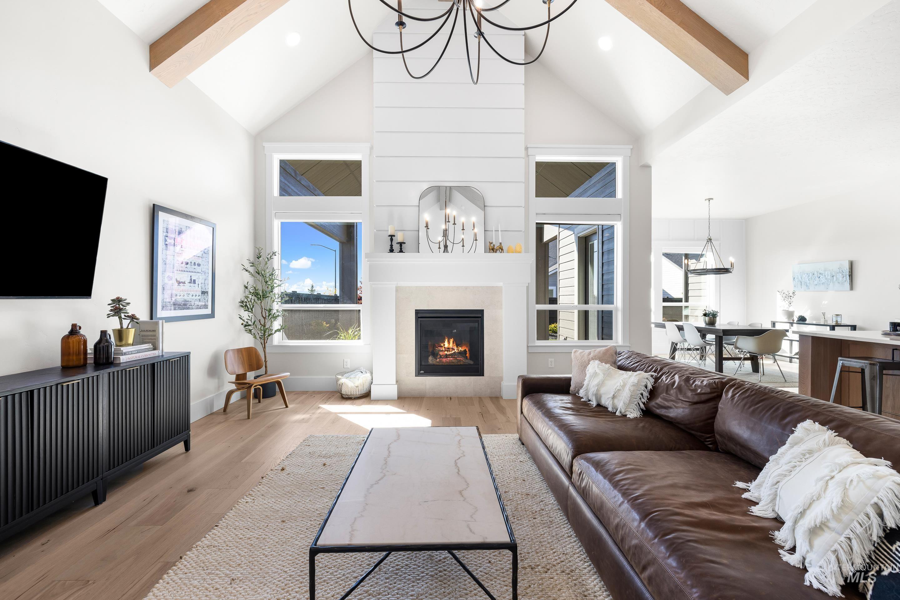 Living area with a chandelier, light wood-style floors, beam ceiling, plenty of natural light, and high vaulted ceiling