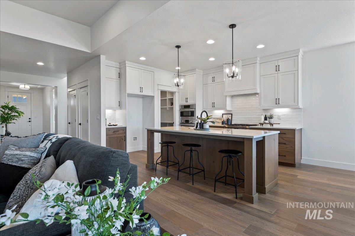 Kitchen featuring white cabinets, a breakfast bar area, open floor plan, decorative light fixtures, and dark wood-style floors