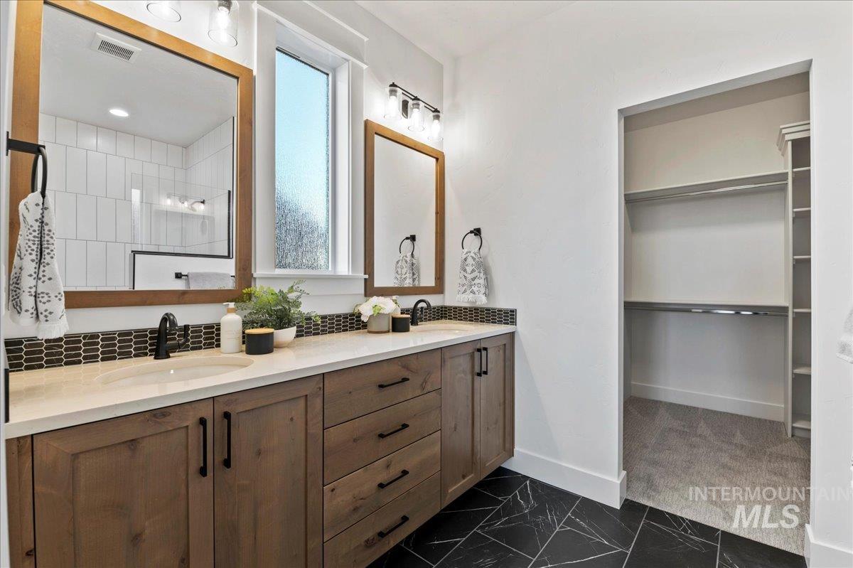 Bathroom with double vanity, dark marble finish flooring, and a walk in closet