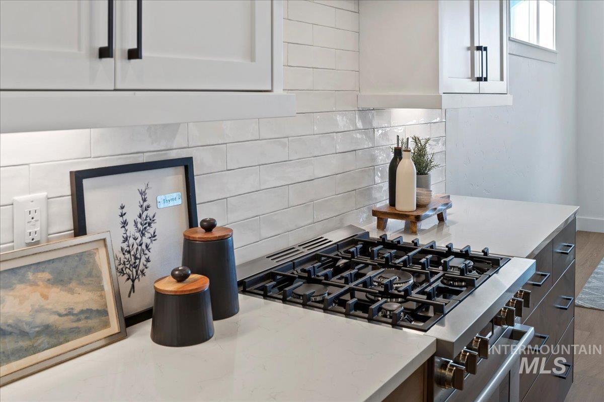 Kitchen featuring backsplash, stainless steel gas stove, white cabinetry, and light stone countertops