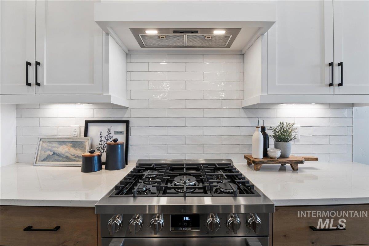 Kitchen featuring exhaust hood, backsplash, and stainless steel gas range oven