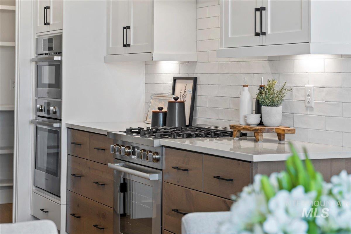 Kitchen with backsplash, appliances with stainless steel finishes, and white cabinetry