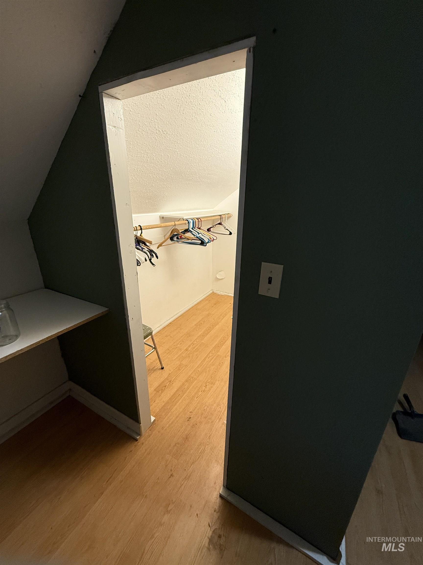 Hall with light wood-style flooring, lofted ceiling, and a textured ceiling