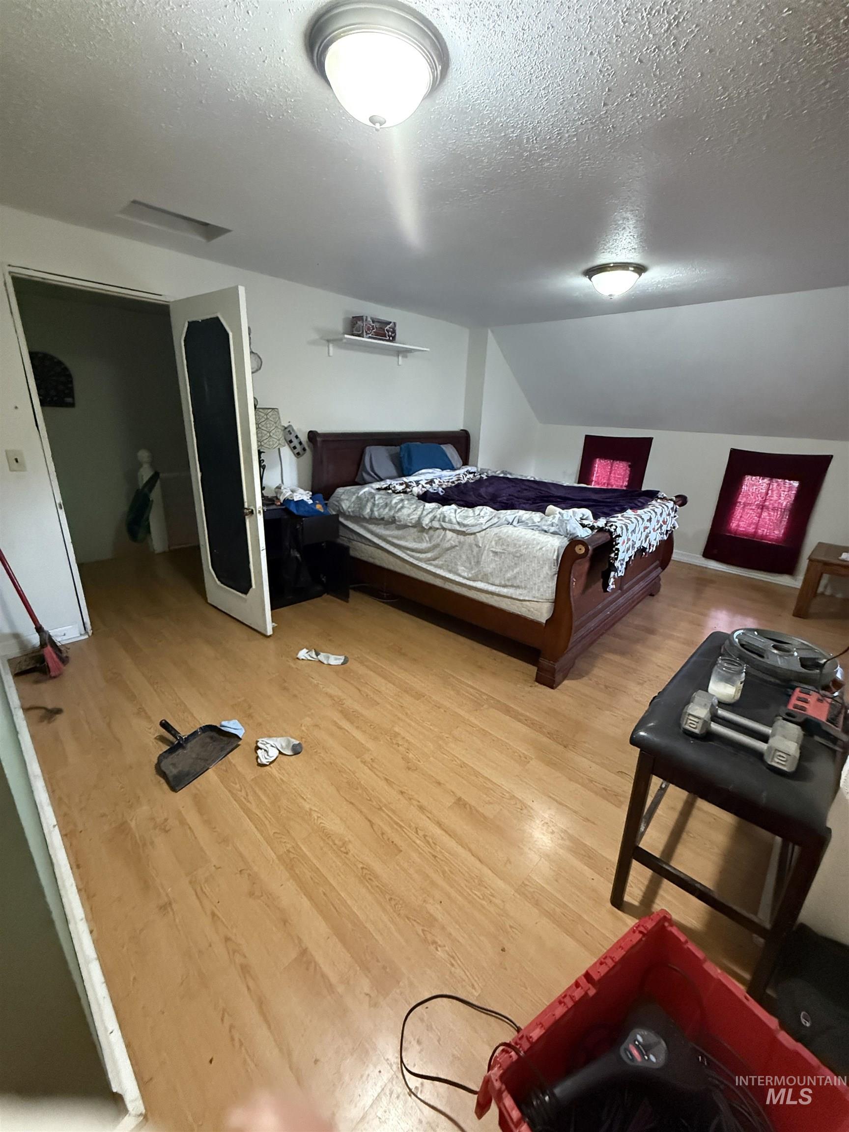 Bedroom with a textured ceiling, light wood finished floors, and lofted ceiling