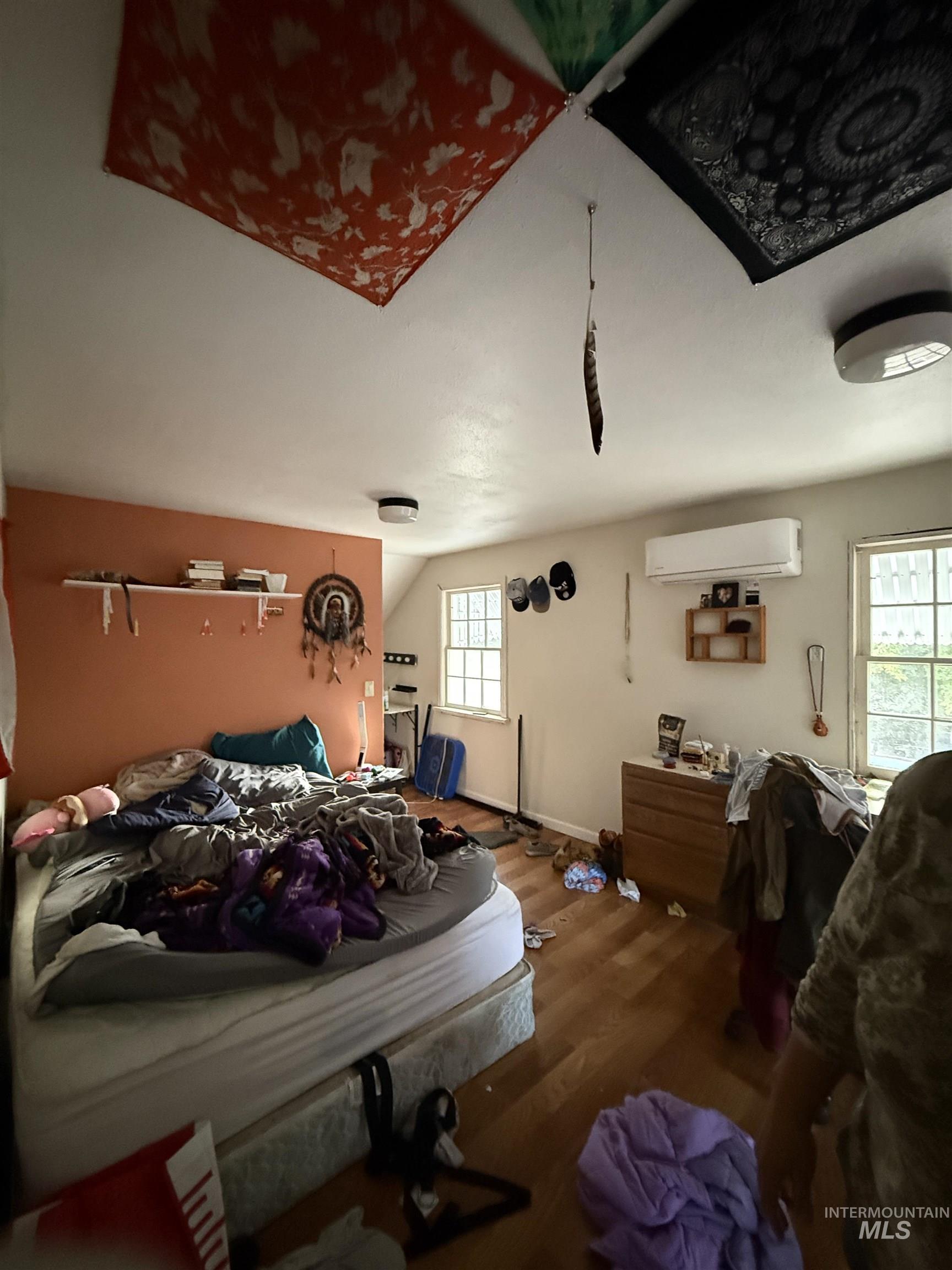 Bedroom featuring wood finished floors, a wall mounted AC, and vaulted ceiling