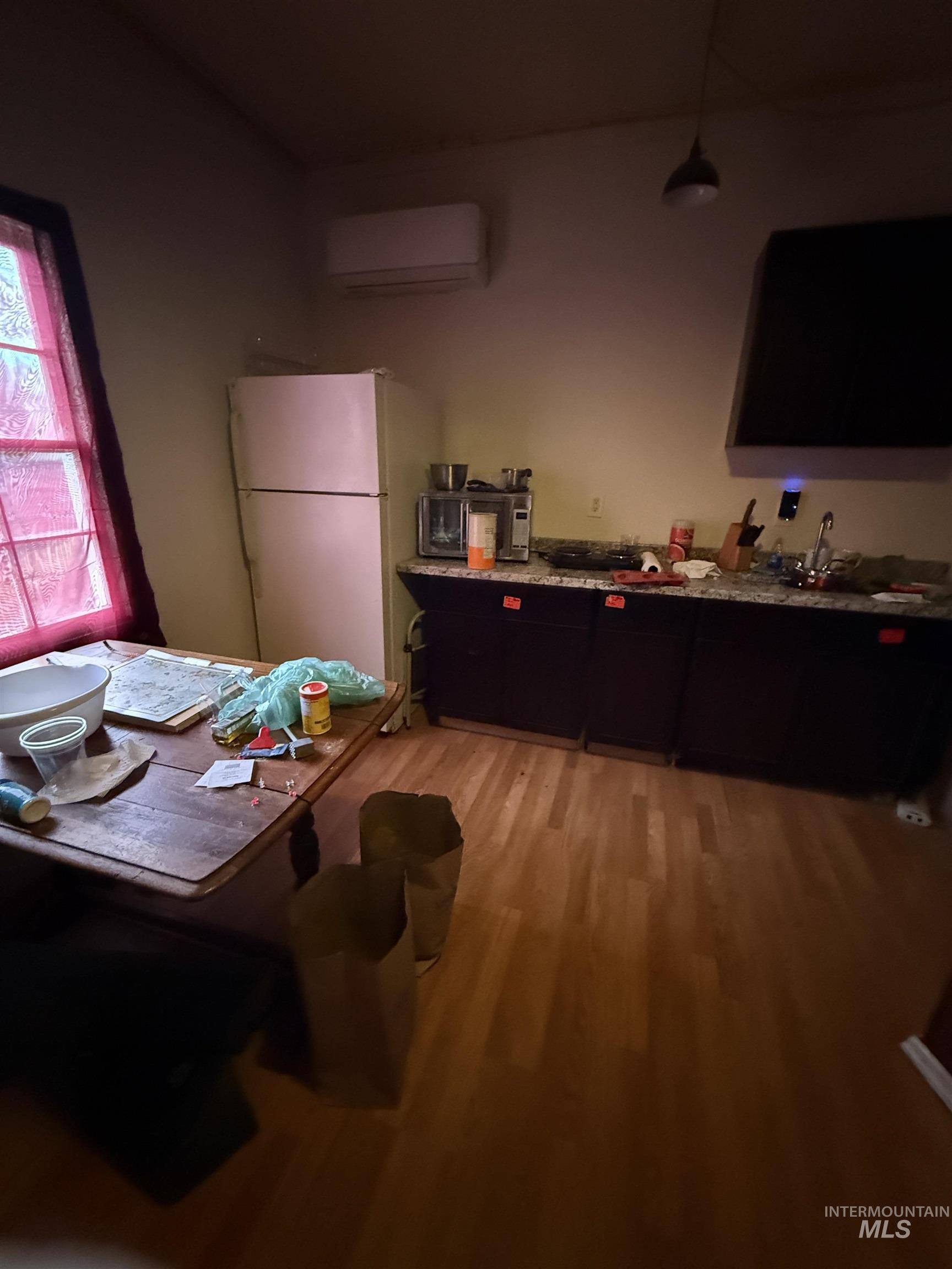 Kitchen with freestanding refrigerator, light wood-type flooring, an AC wall unit, dark cabinetry, and hanging light fixtures