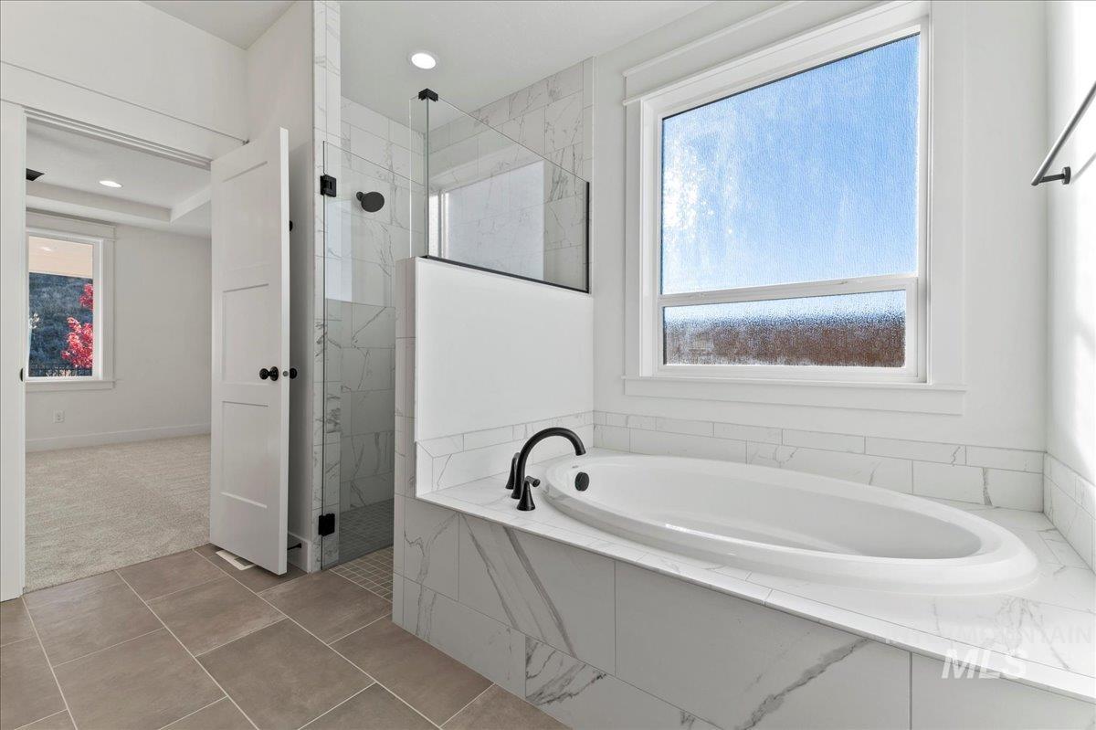 Full bath featuring a garden tub, a marble finish shower, light tile patterned floors, and light colored carpet