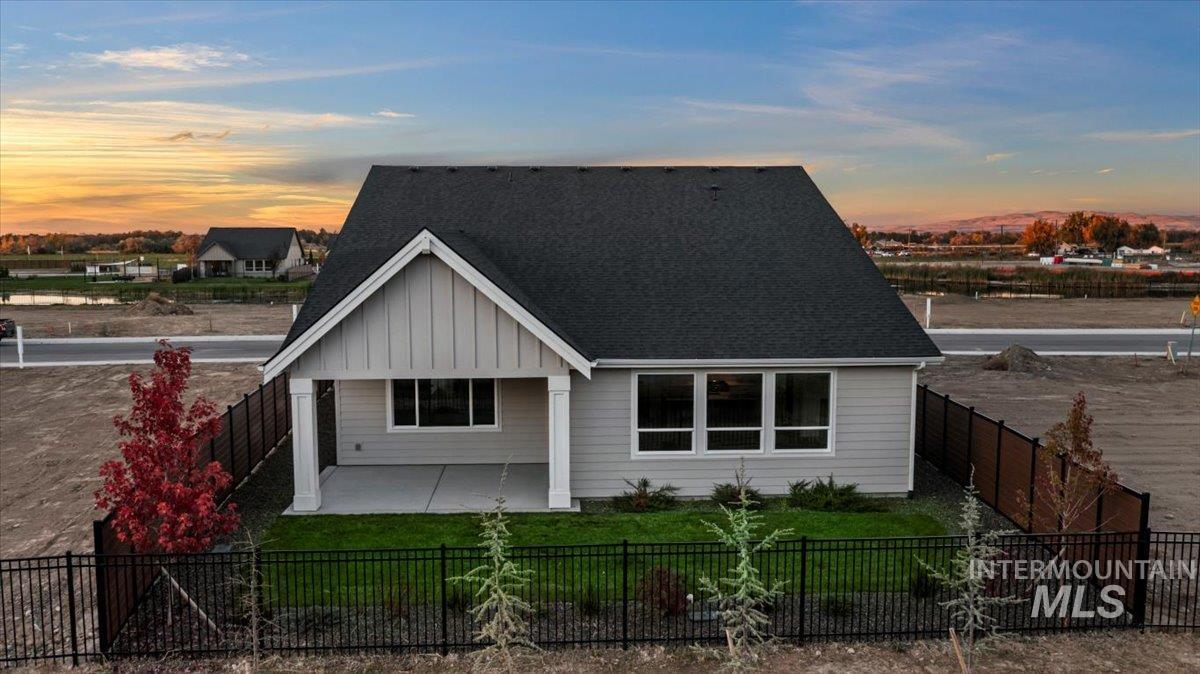 View of front of home with board and batten siding, a fenced backyard, and a shingled roof
