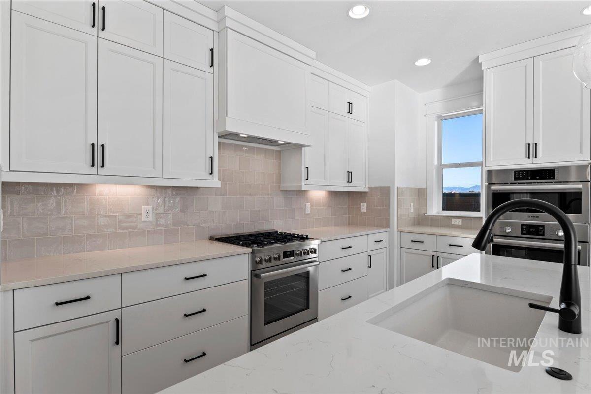 Kitchen featuring white cabinetry, stainless steel appliances, backsplash, light stone counters, and recessed lighting