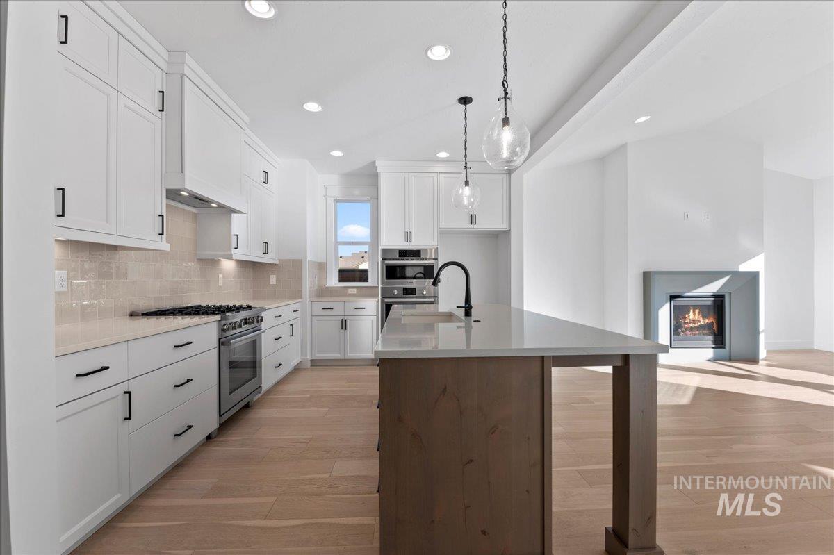 Kitchen featuring light wood-type flooring, recessed lighting, stainless steel appliances, tasteful backsplash, and white cabinetry