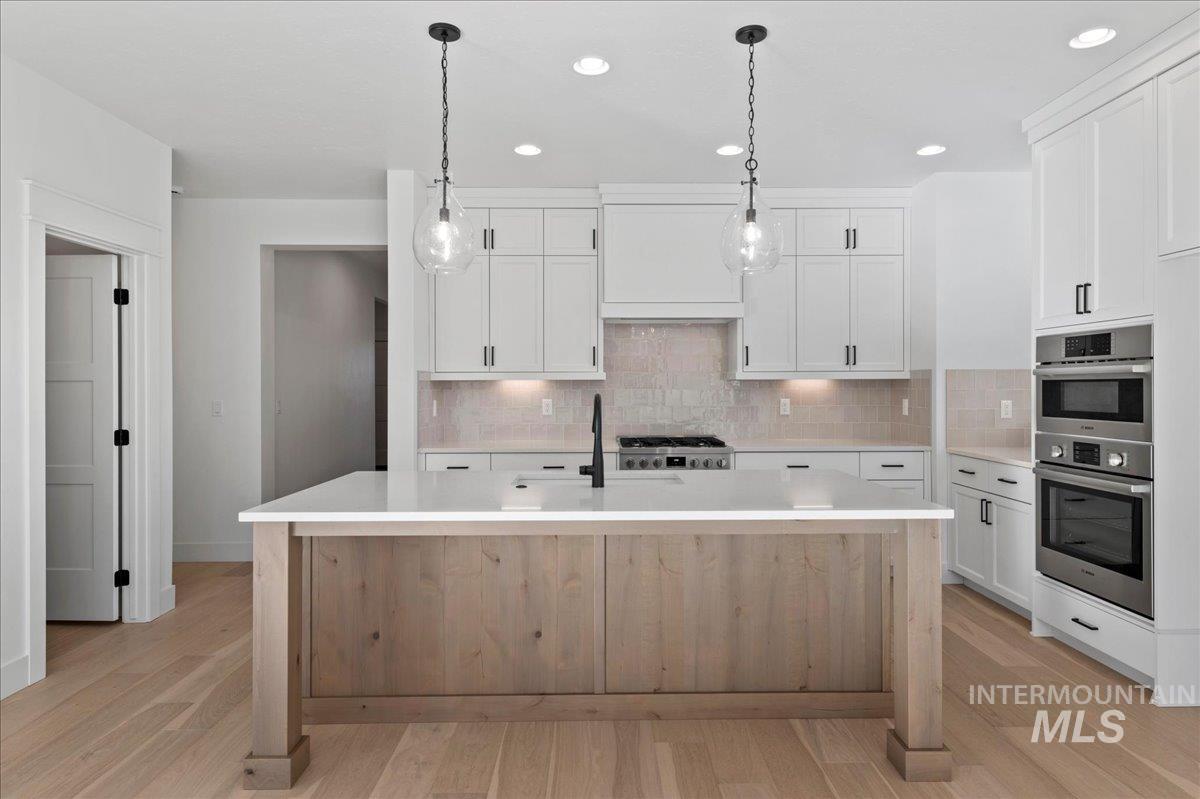 Kitchen with tasteful backsplash, white cabinets, a kitchen island with sink, recessed lighting, and light wood-style floors