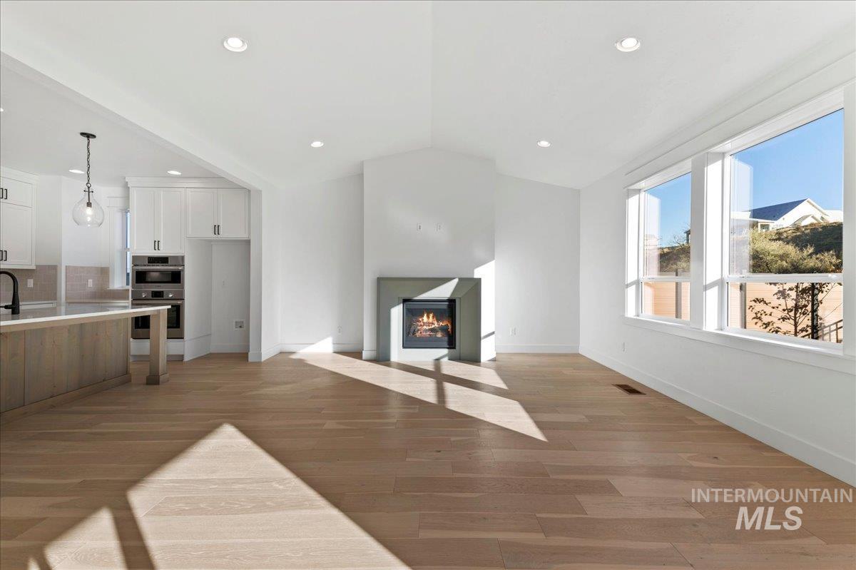 Unfurnished living room with a fireplace with flush hearth, light wood-style floors, lofted ceiling, and recessed lighting