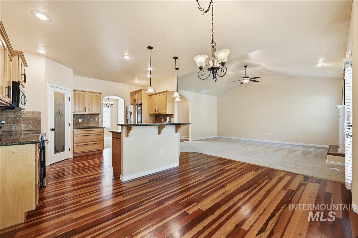 Kitchen with a kitchen breakfast bar, arched walkways, open floor plan, dark wood finished floors, and hanging light fixtures