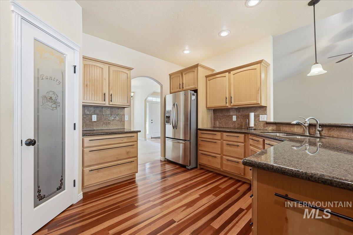 Kitchen featuring light brown cabinetry, arched walkways, stainless steel fridge, pendant lighting, and recessed lighting