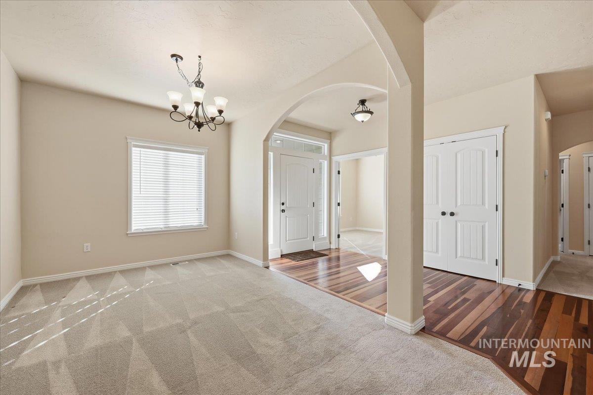 Carpeted empty room featuring arched walkways, a chandelier, and wood finished floors