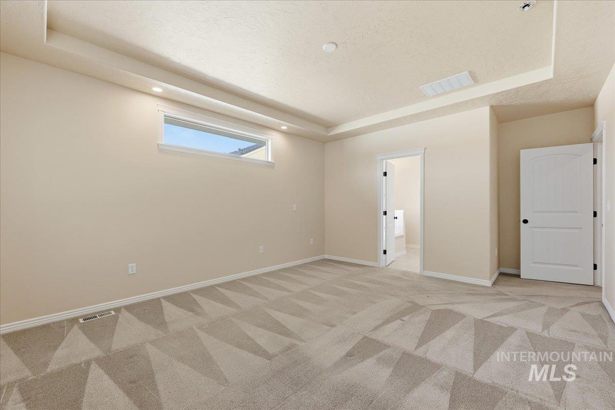 Unfurnished bedroom with a raised ceiling, light colored carpet, a textured ceiling, connected bathroom, and recessed lighting