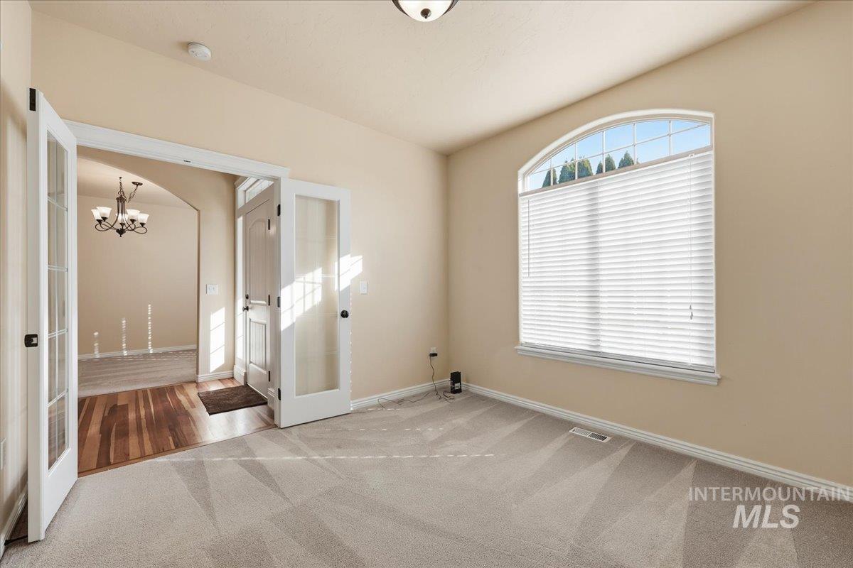 Carpeted spare room featuring french doors and a chandelier