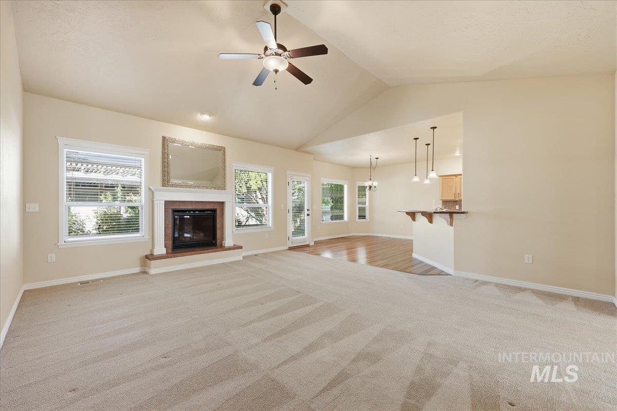 Unfurnished living room featuring a glass covered fireplace, light colored carpet, ceiling fan, and high vaulted ceiling