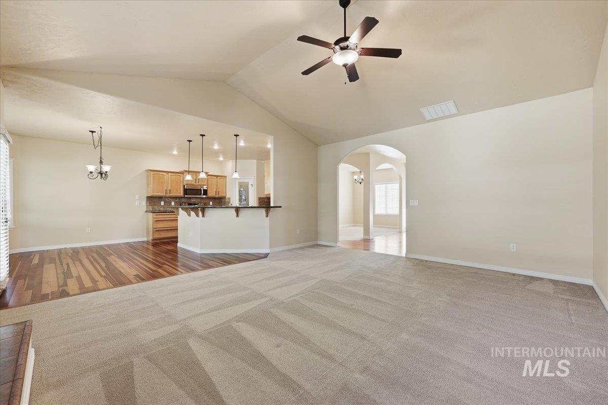 Unfurnished living room featuring vaulted ceiling, dark colored carpet, arched walkways, a chandelier, and dark wood-style flooring