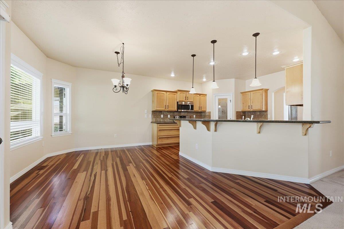Kitchen featuring backsplash, a breakfast bar, hanging light fixtures, a chandelier, and dark stone counters
