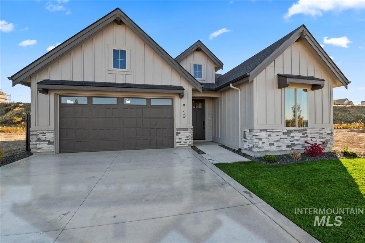 Modern farmhouse with board and batten siding, stone siding, driveway, and a front lawn